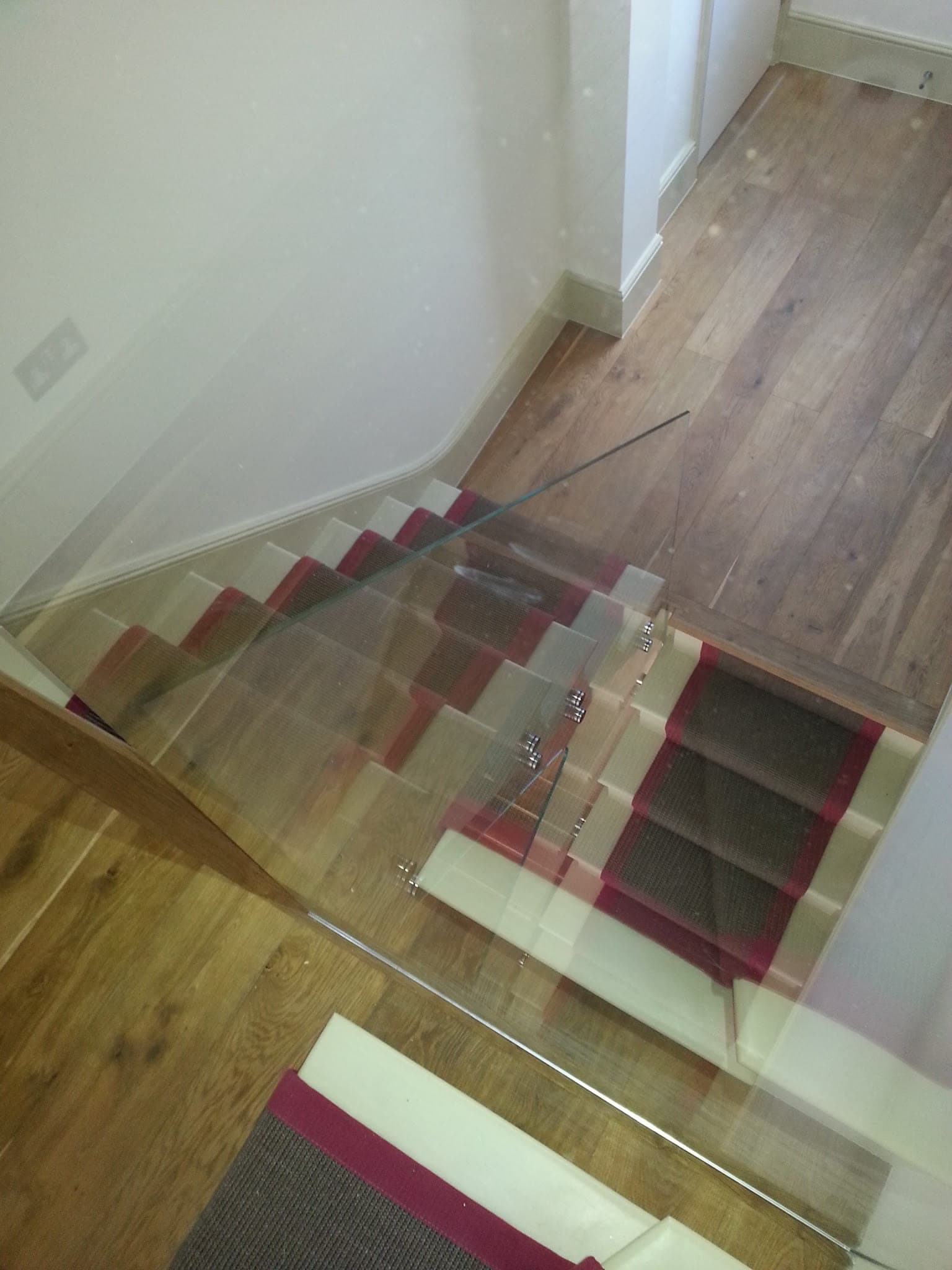 Looking down a staircase with a glass balustrade to the timber floor below