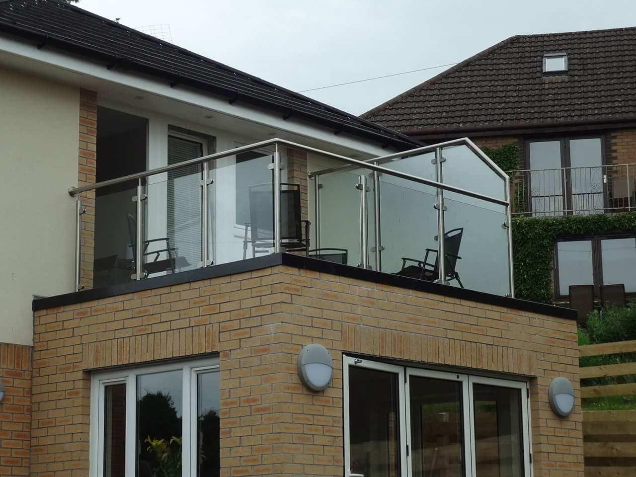 Exterior balcony with glass infill panels and a metal top rail on a brick house