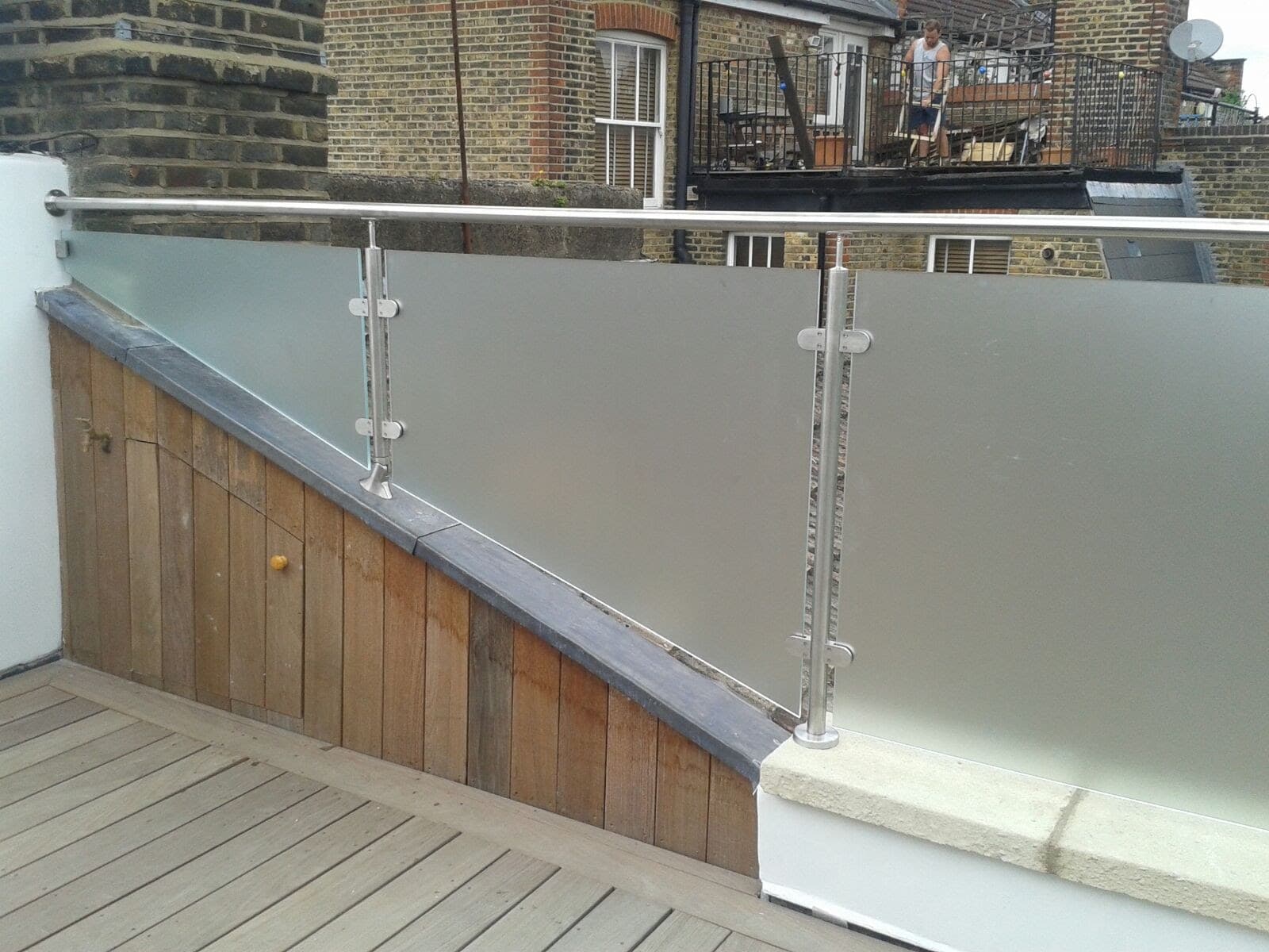 Roof terrace balustrade in obscured privacy glass with metal posts and handrail, against brickwork