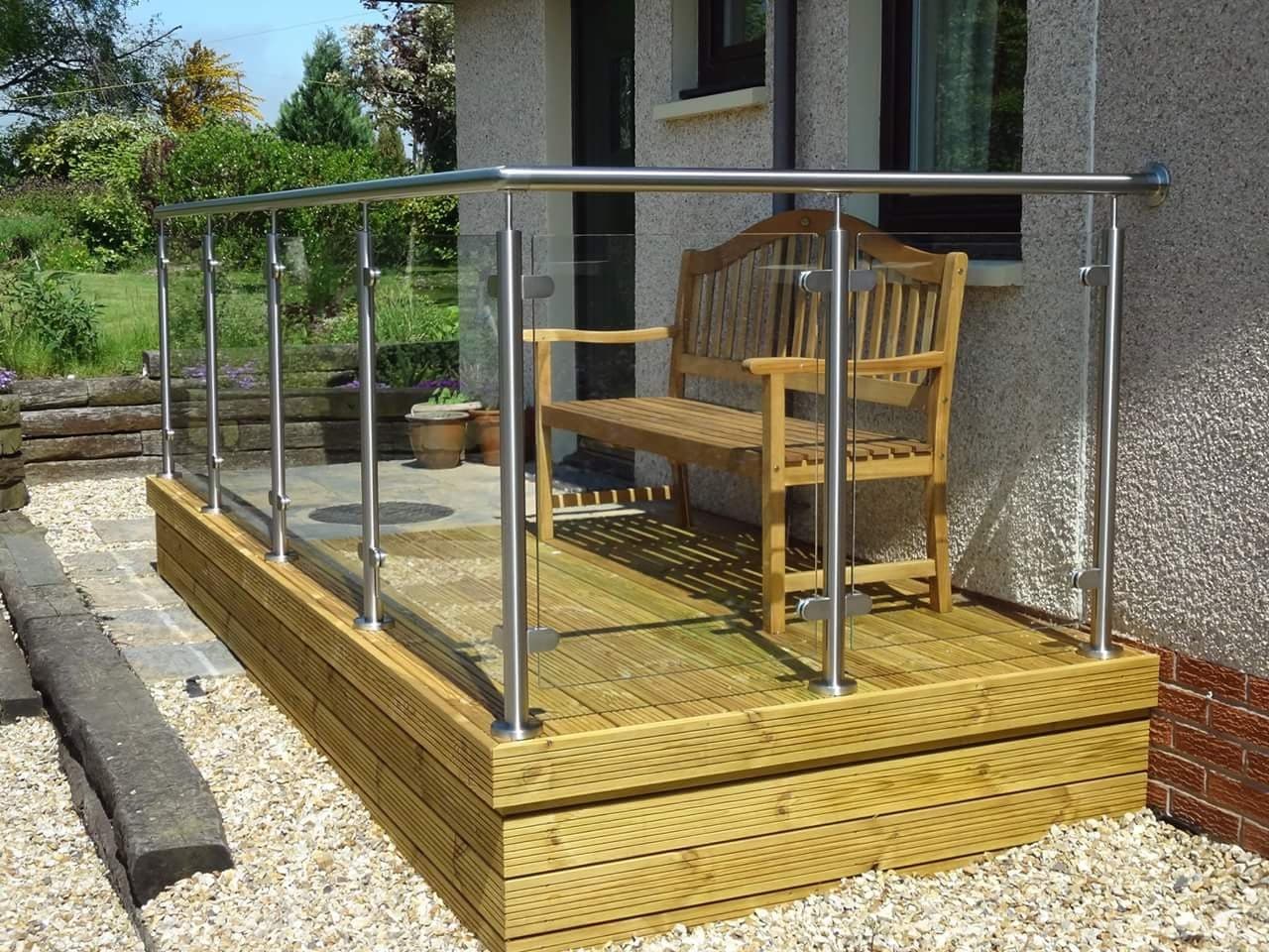 Glass balustrade with metal posts and a handrail enclosing a raised timber deck in a garden