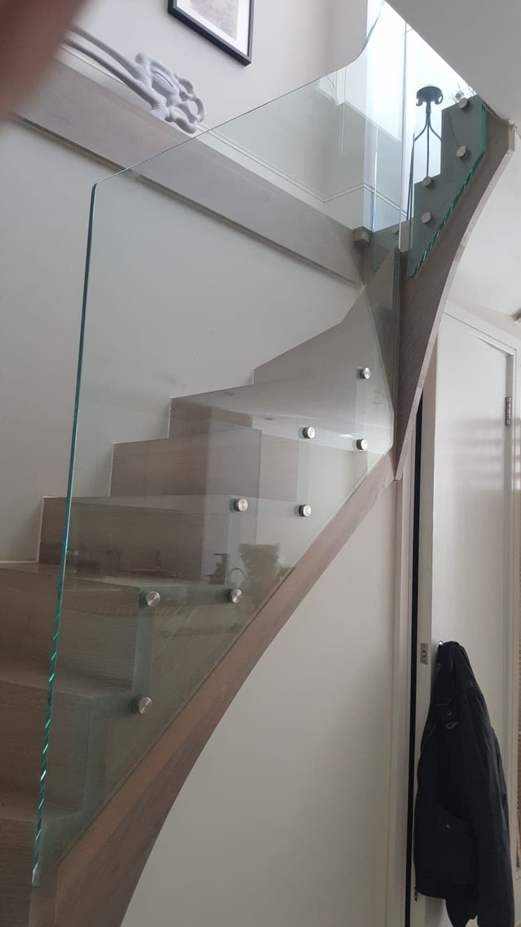 Interior staircase with a frameless glass balustrade fixed by round standoff bolts against a curved wall