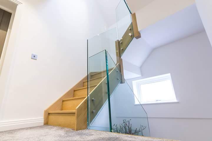 Loft staircase with a glass balustrade panel beside timber treads, lit by a rooflight above