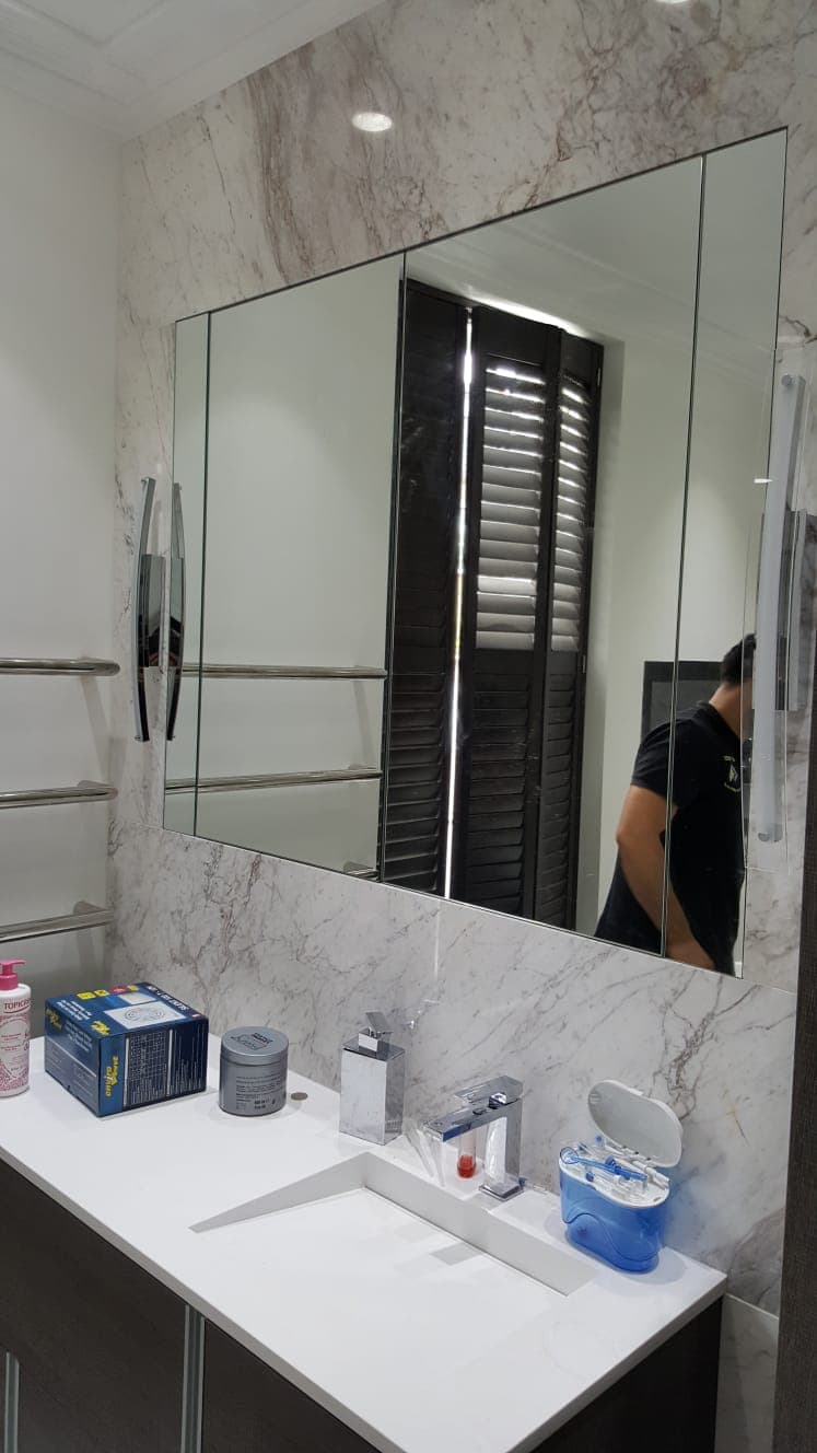 Large bathroom mirror on a stone-tiled wall, cut around a heated towel rail