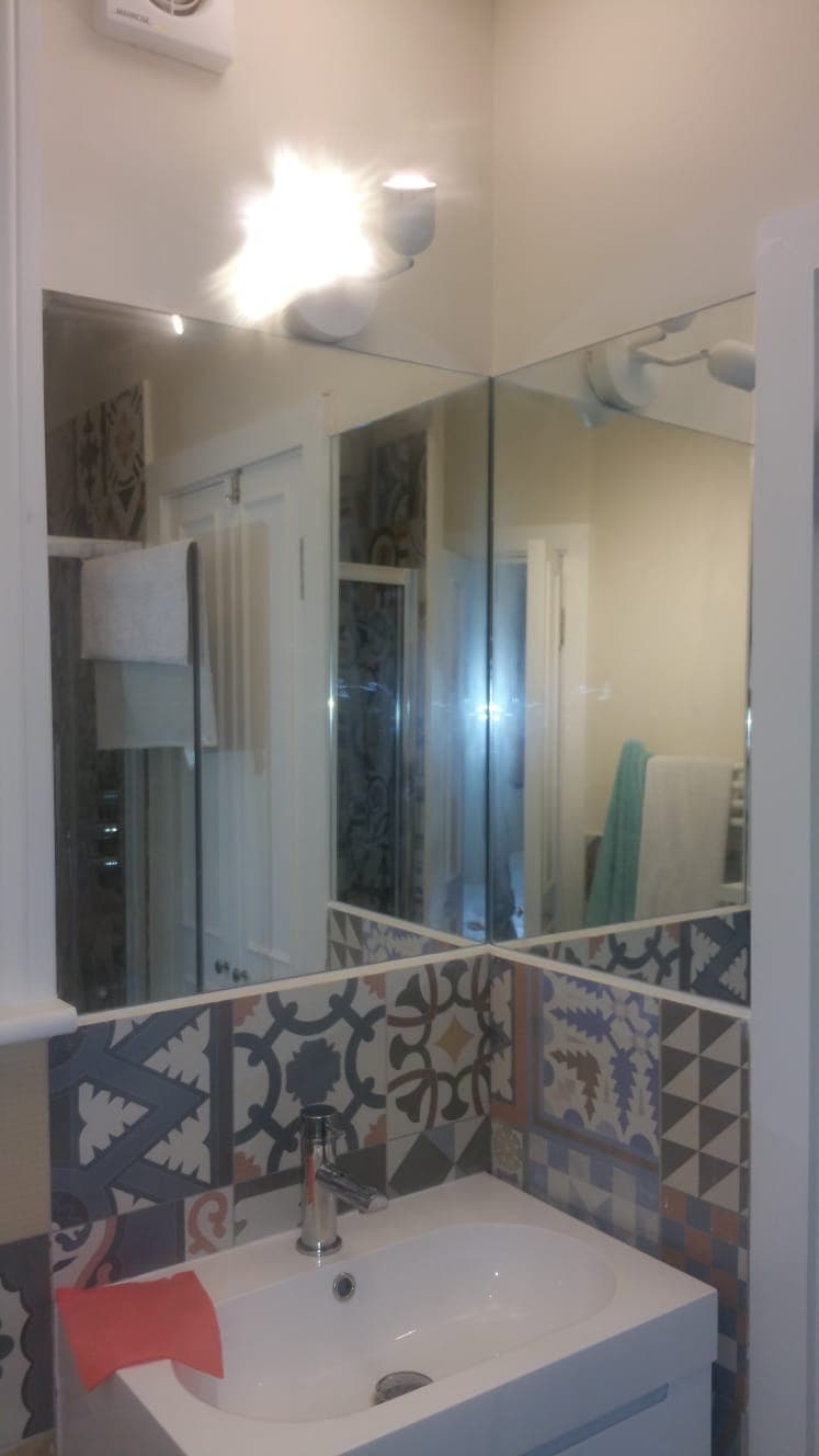 Mirror panel above a tiled bathroom wall, reflecting the patterned floor tiles opposite