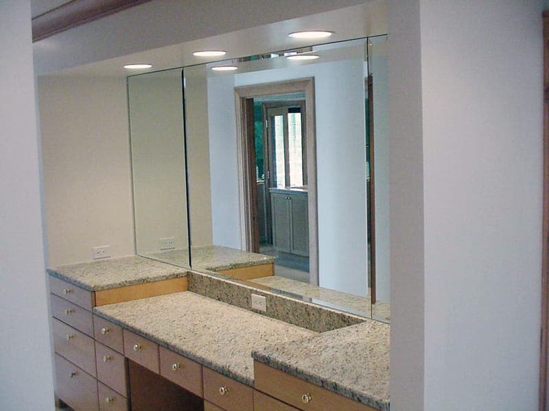 Wide mirror above a stone-topped vanity unit lit by downlights