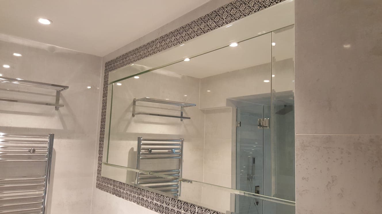 Bathroom mirror with a patterned mosaic border above a heated towel rail