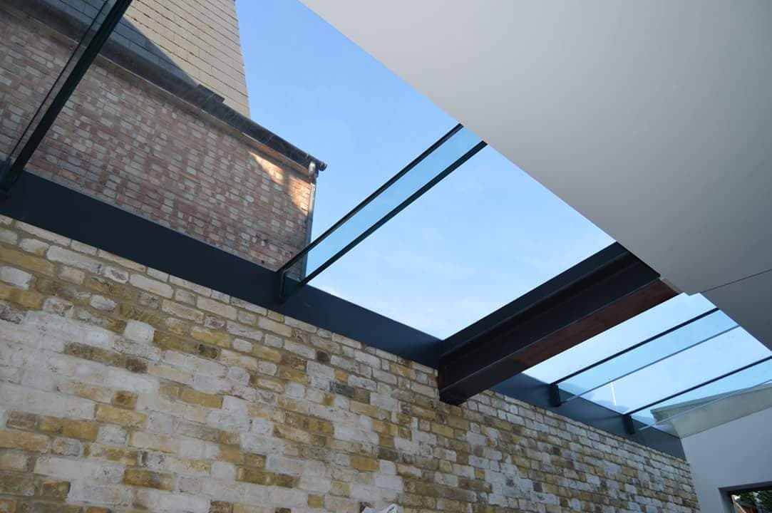 A glazed roof carried on steel beams over a side return, seen from inside against exposed brickwork