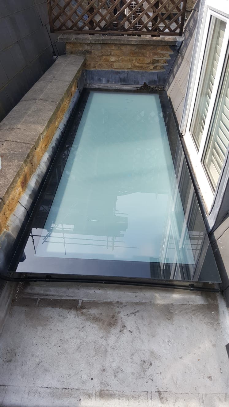A long slim rooflight on a flat roof beside shuttered windows