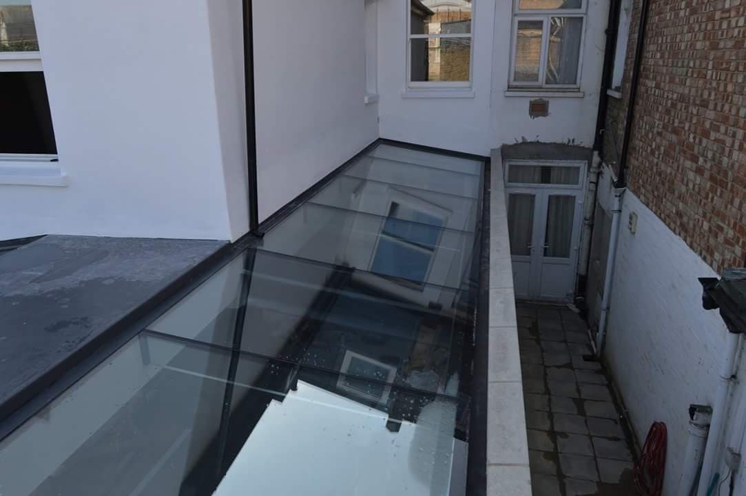 Dark-framed glazed panels set into the ground beside a doorway, glazing a lightwell