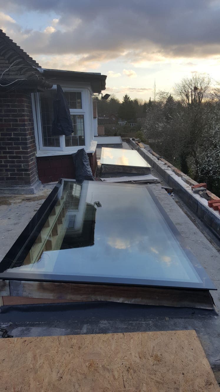 A large rooflight on a flat roof reflecting the sky, with the house wall behind