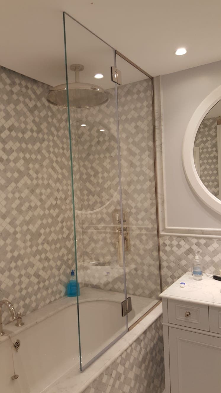 Frameless shower panel against mosaic tiling, with a round mirror on the wall beyond