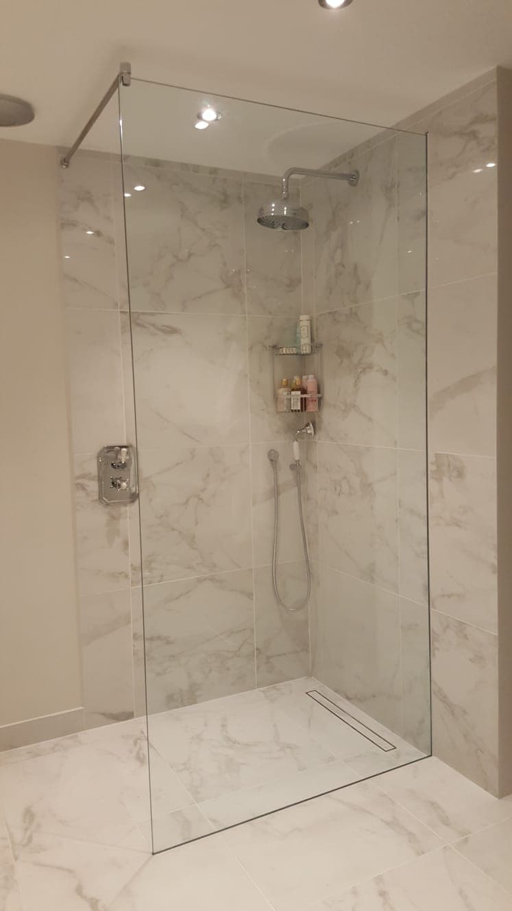 Walk-in shower panel in large-format marble-effect tiling, with chrome wall brackets
