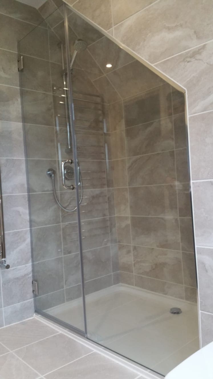 Hinged shower door and inline panel in a grey stone-tiled bathroom
