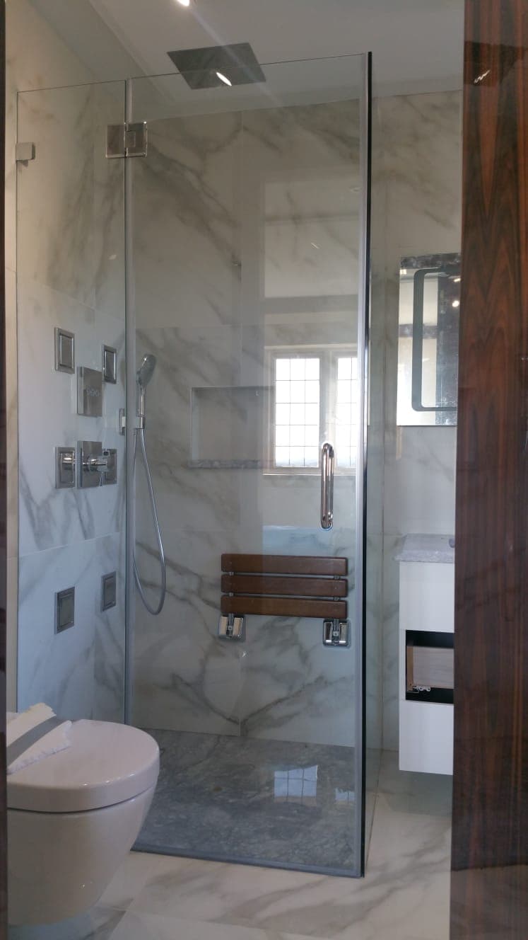 Hinged shower enclosure in book-matched stone tiling, with a folding timber seat