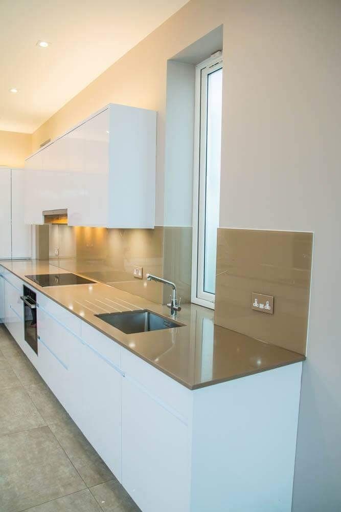Bronze-toned coloured glass splashback running the length of a white gloss kitchen behind the hob and sink