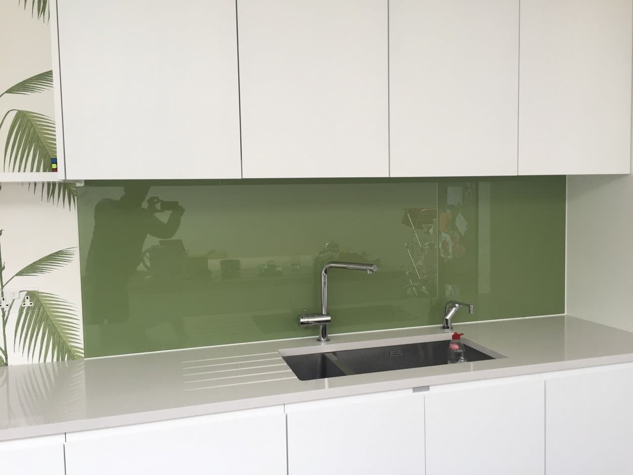 Olive green glass splashback behind an inset sink and mixer tap