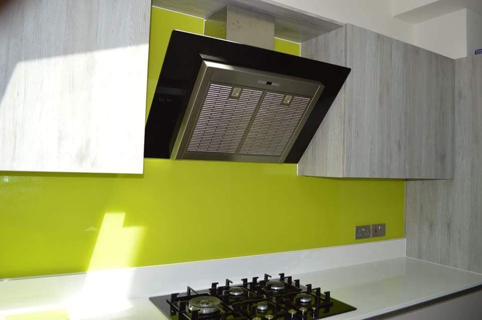 Lime green glass splashback cut around an angled extractor hood above a gas hob