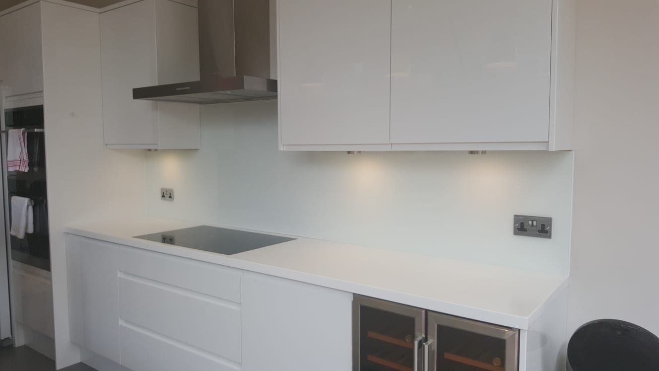 Pale glass splashback behind an induction hob beneath a chimney extractor