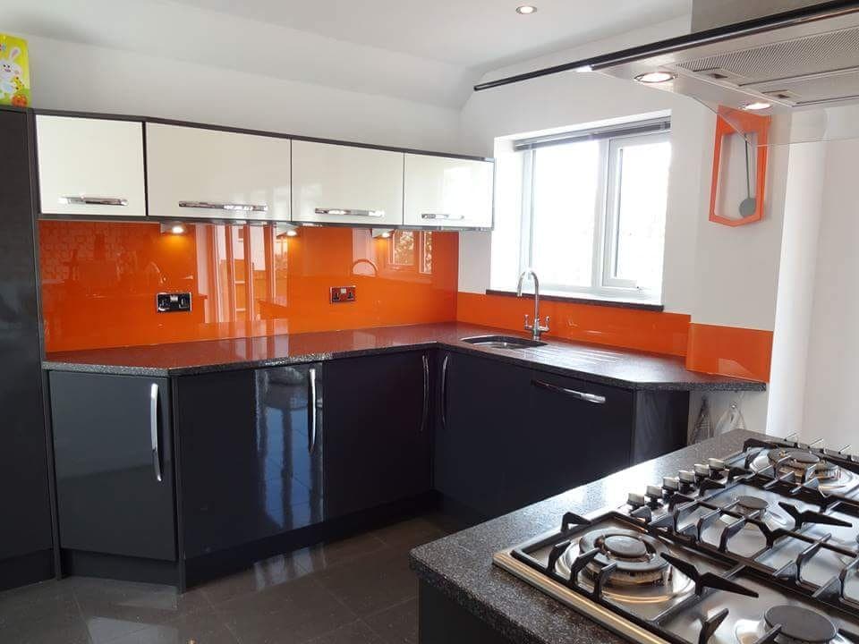 Orange glass splashback in a kitchen with dark gloss units and a gas hob