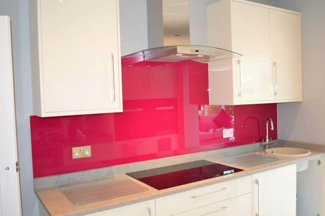 Deep pink glass splashback behind an induction hob under a curved glass extractor hood