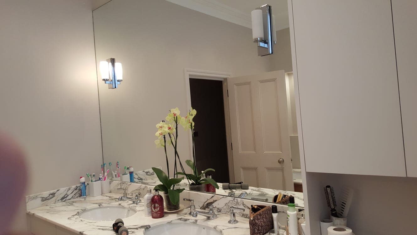 Full-height mirror beside a stone vanity with wall lights and orchids